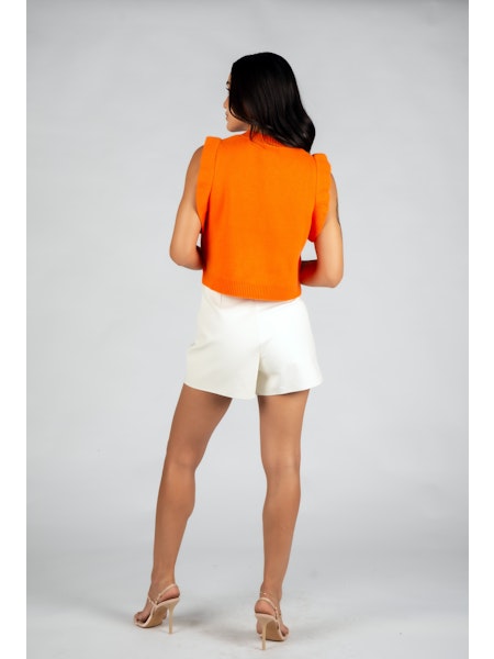 Woman wearing an orange sleeveless top and white shorts on a gray background