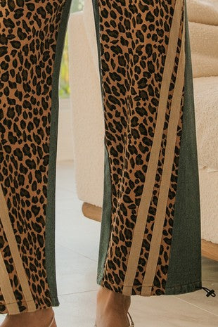 Close-up of wide-leg pants featuring a leopard print front, denim side panels, tan racing stripes, and adjustable toggle hem, styled for Sloan’s Formal Boutique.