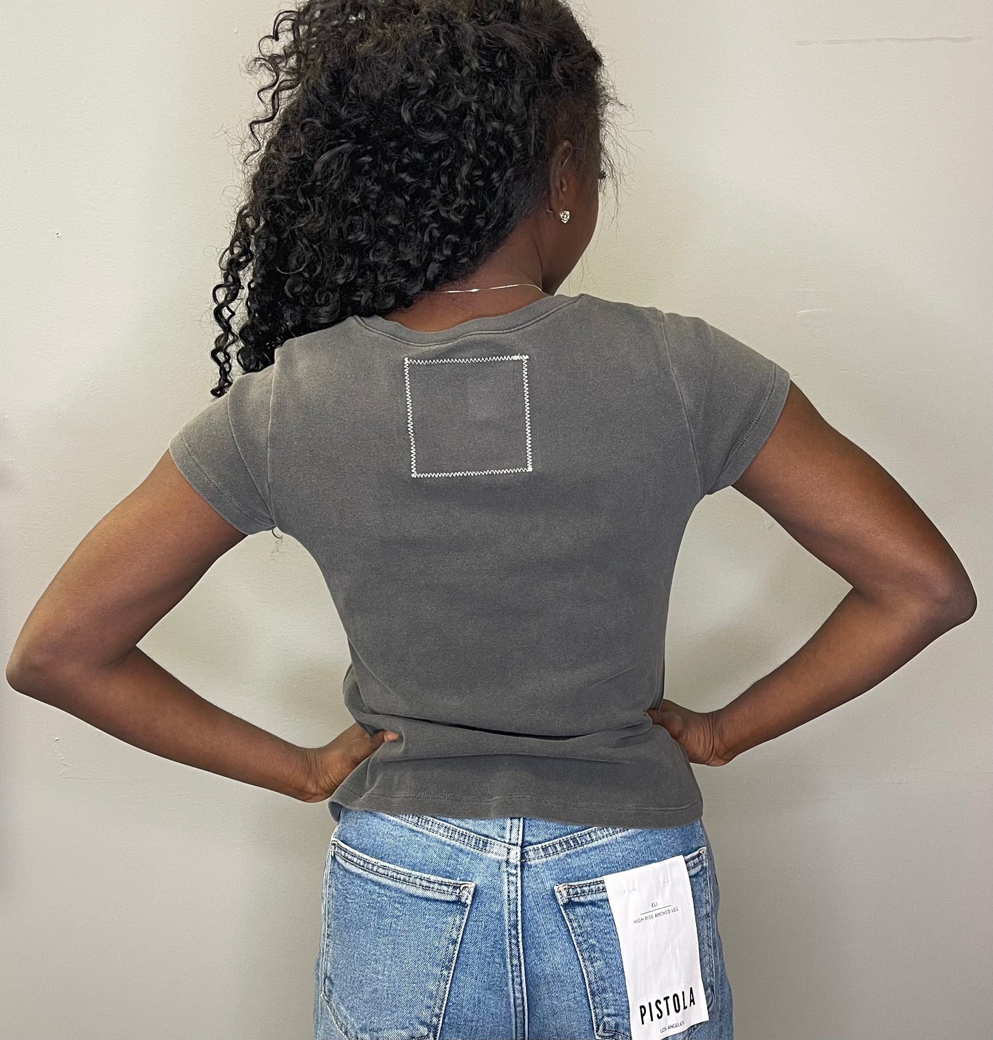 Back view of the model showing the plain back of the charcoal graphic tee with subtle stitched square detail near the neckline and rolled sleeves