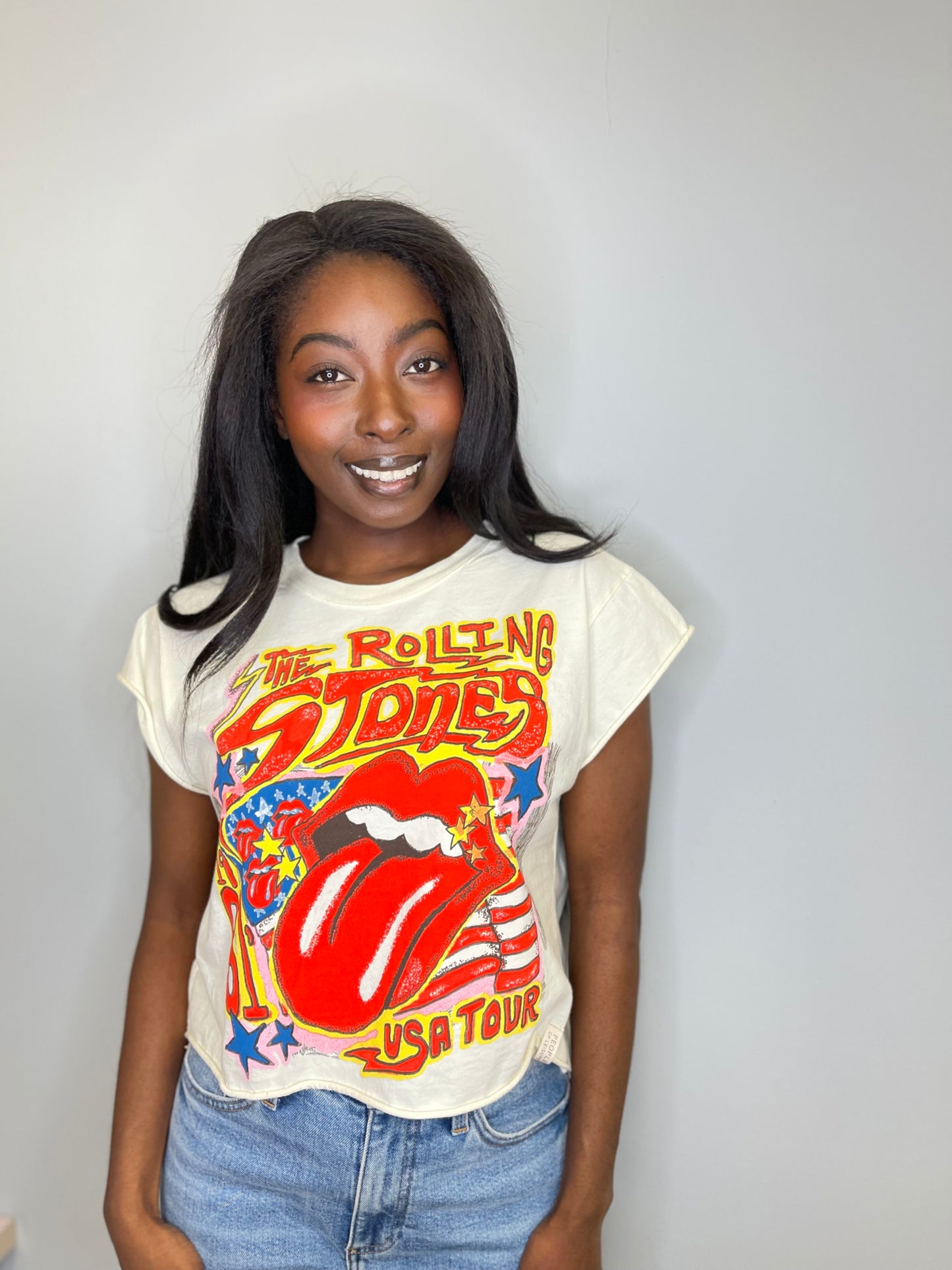 Full front view of a model standing confidently with the Rolling Stones tee tucked into high-rise jeans, displaying the vibrant front graphic and the tee’s cropped length.