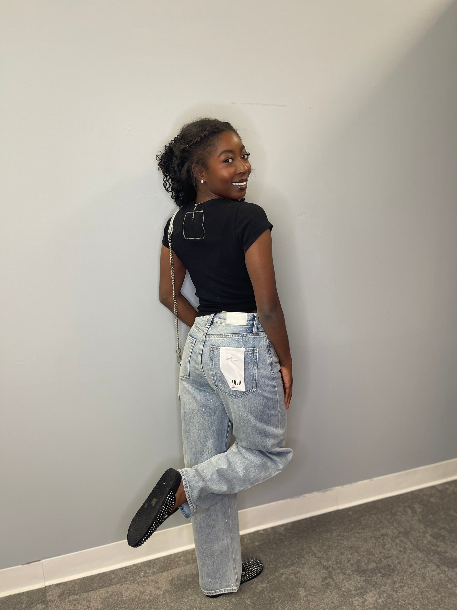 Back view of the model in the fitted tee, showing the stitched square label detail and a playful pose with one leg up, highlighting the relaxed yet stylish vibe.