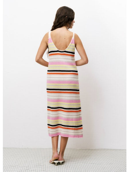 Model wearing the Alcathea Dress, shown from the back, featuring a deep scoop back and colorful horizontal stripes in pink, yellow, orange, black, and ivory. The dress is midi-length with a fitted silhouette, styled with open-toe sandals against a white background.