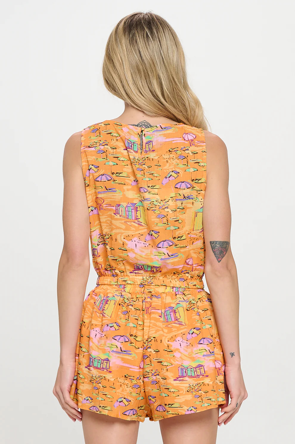 Back view of a woman wearing a sleeveless golden-orange matching set featuring a coastal beach print with umbrellas and beach huts, and an elastic waist.