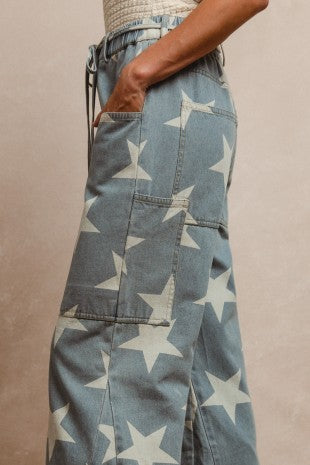 Side view of a woman wearing wide-leg denim jeans with a bold ivory star print, featuring large front pockets and a drawstring waist, styled for Sloan's Boutique.
