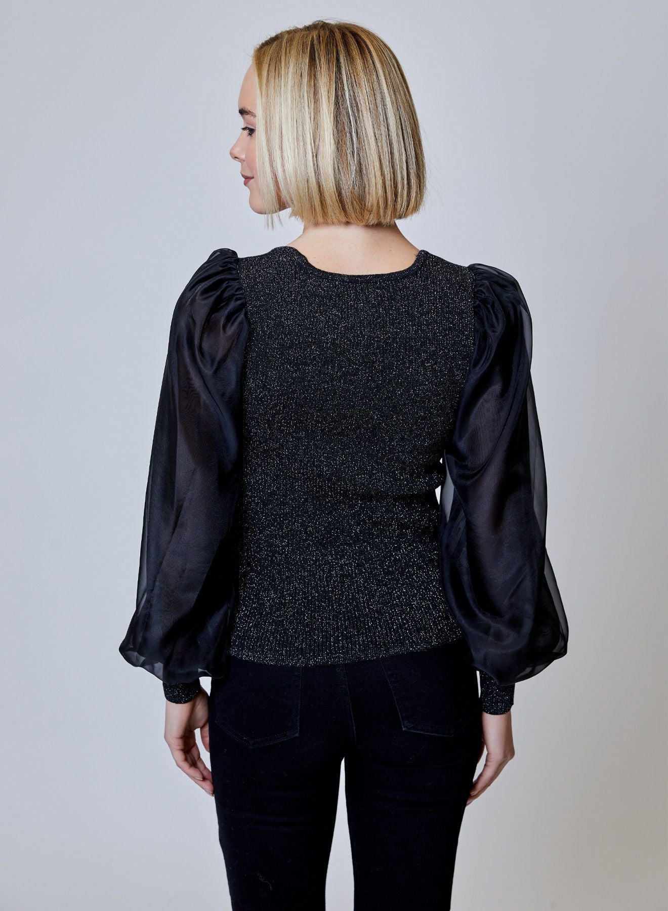 Model wearing the Maxine Blouse in black glitter fabric, featuring a sweetheart neckline, sheer sleeves, and subtle shimmer detailing.