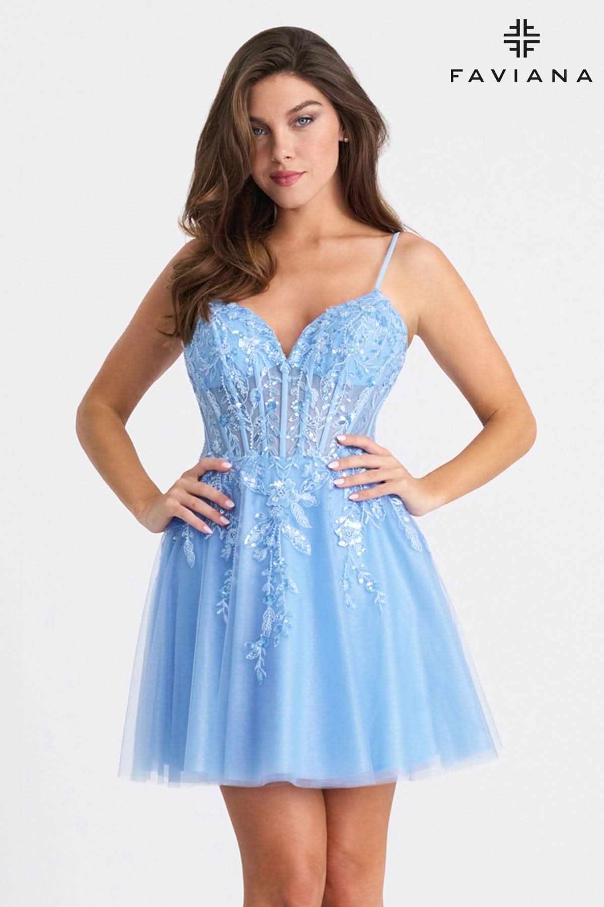 Woman wearing a light blue dress with floral embroidery, standing against a white background with Faviana logo.