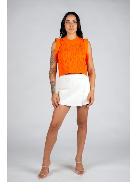 Woman wearing an orange sleeveless top and white skirt on a gray background