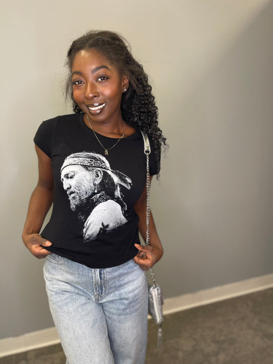 Model smiles confidently in a black fitted tee featuring a monochrome portrait of Willie Nelson, paired with light-wash jeans and a silver chain purse.