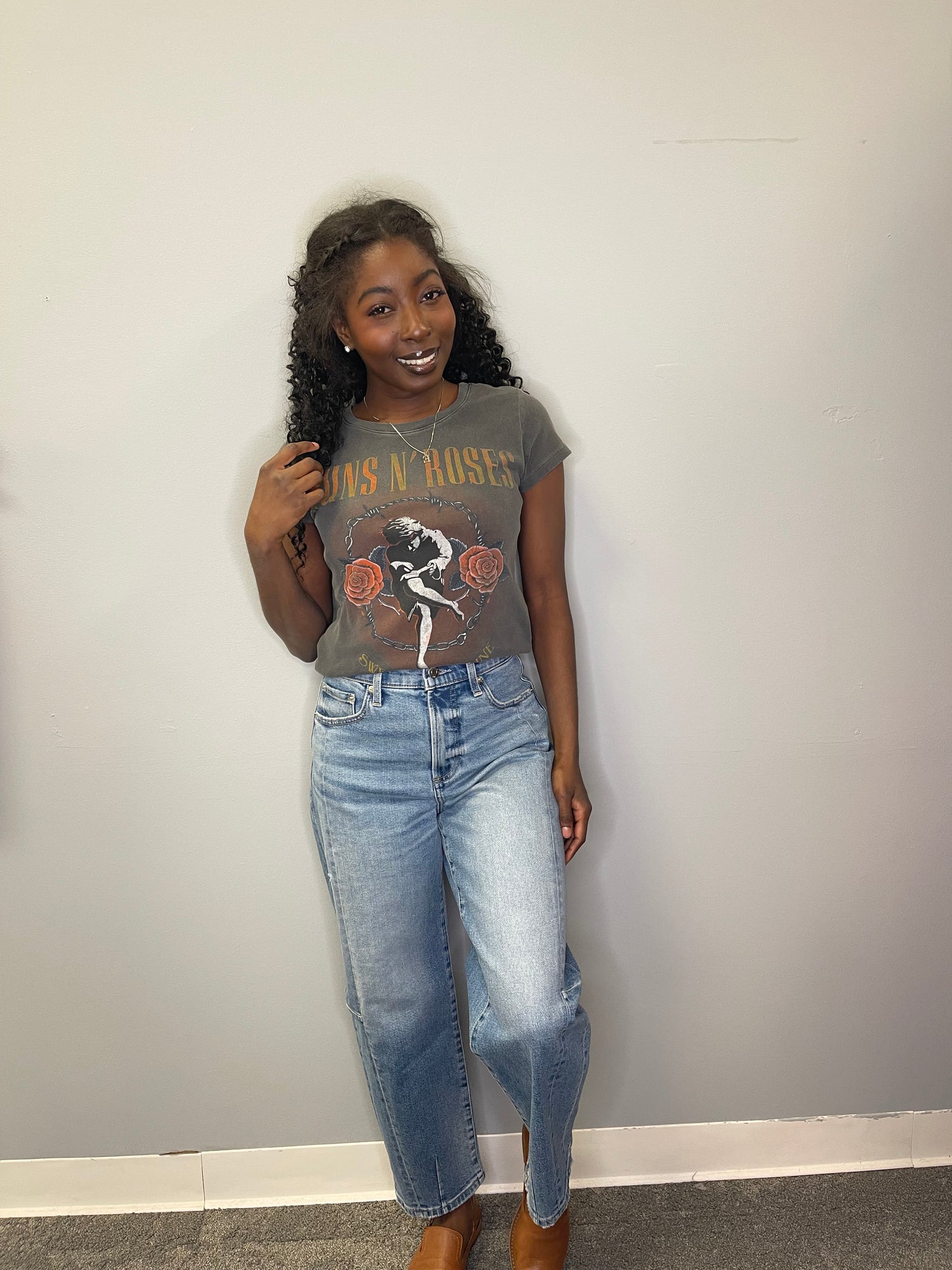 Model poses smiling with one hand in her hair, wearing the charcoal cropped Guns N’ Roses “Sweet Child O’ Mine” graphic tee and high-waisted jeans.