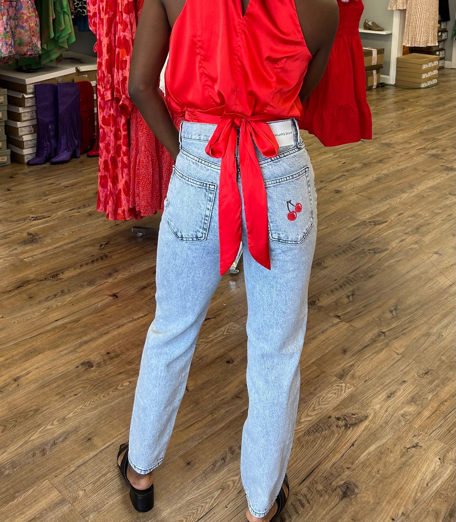 Model wearing Cherry Bomb Jeans in light blue denim with cherry on pocket, featuring a high-rise waist, wide leg fit, and raw hem detailing.