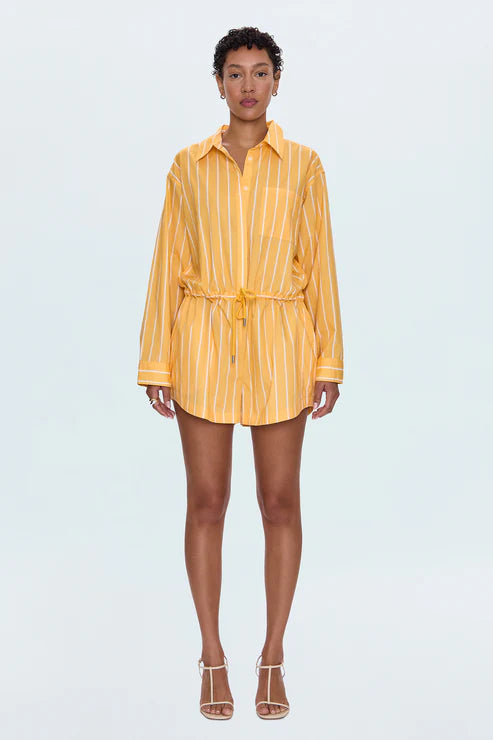 Front view of a woman wearing the Pistola Amelie Romper in yellow with white vertical stripes, featuring long sleeves, a collared neckline, button front, and an adjustable drawstring waist, styled with white strappy heels at Sloan’s Formal Boutique.









