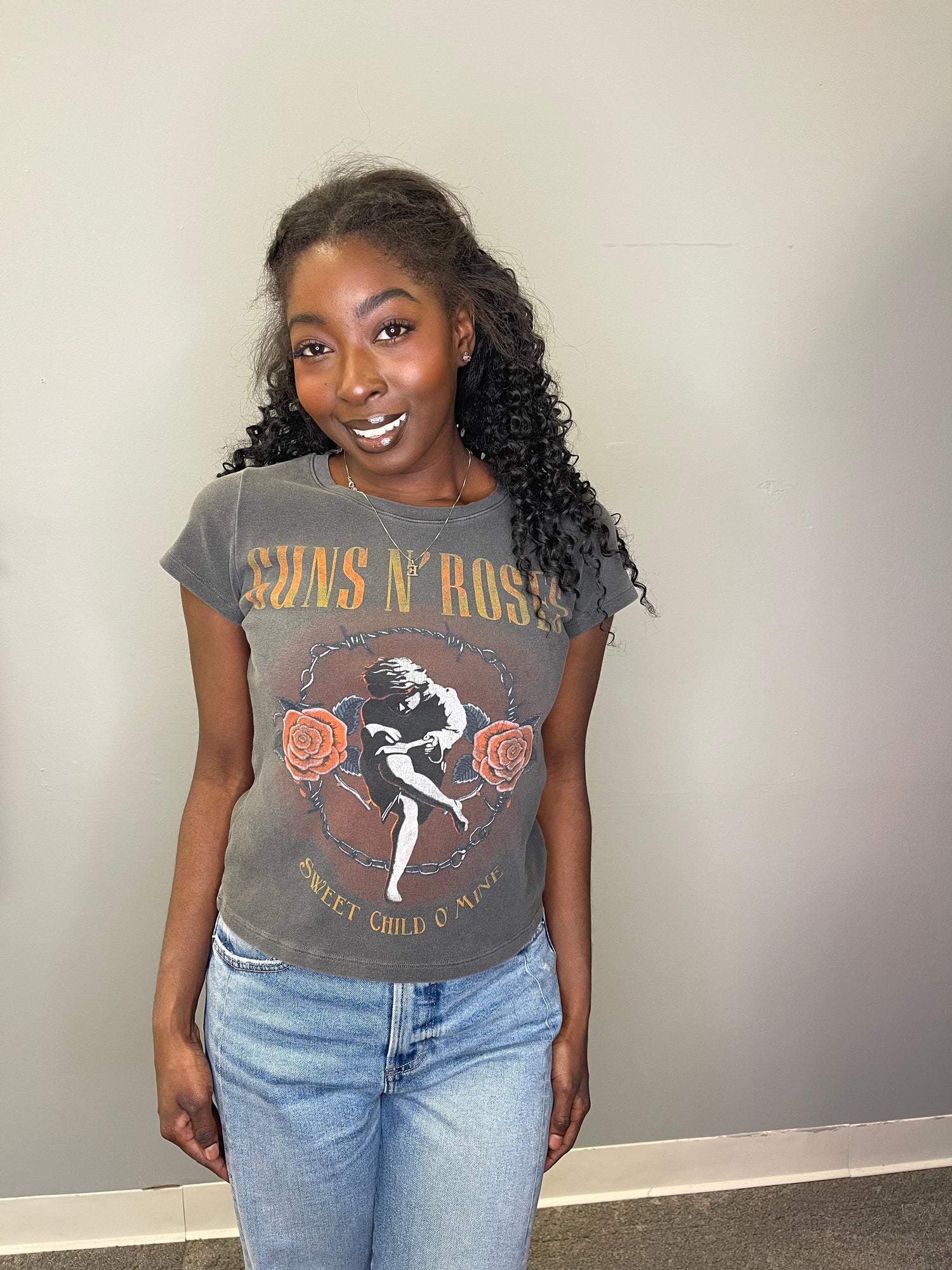 Front-facing close-up of the model smiling in the cropped Guns N’ Roses tee, showing off the vintage wash, feminine graphic, and bold rose details.