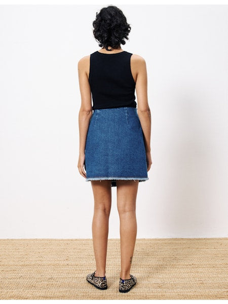 Back view of a woman wearing a high-rise medium-wash denim wrap skirt with raw hem, paired with a black tank top and leopard flats.