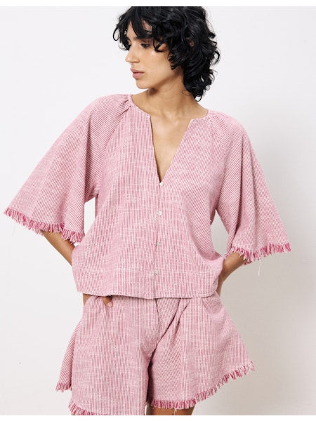 Front view of a woman modeling the Berry Breeze Blouse by FRNCH, featuring elbow-length wide sleeves, a deep V-neckline, and fringe trim in a raspberry micro-stripe