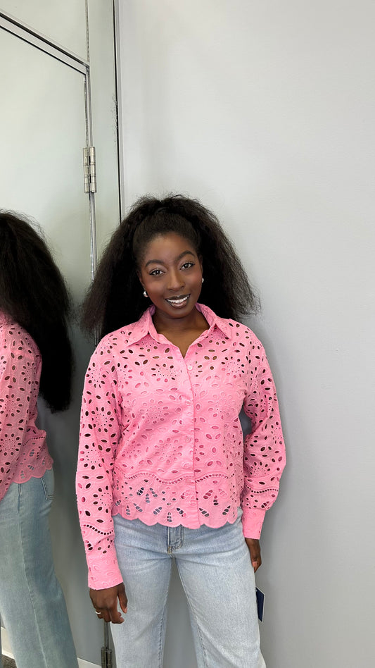 Woman wearing a bright pink floral eyelet blouse layered over a pink tank top, paired with jeans, smiling and posing in a boutique setting.