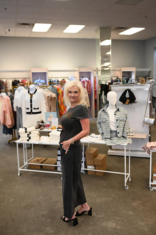 Woman wearing a washed charcoal Guns N' Roses graphic tee with wide-leg black denim and open-toe black heels, standing confidently in a boutique setting.