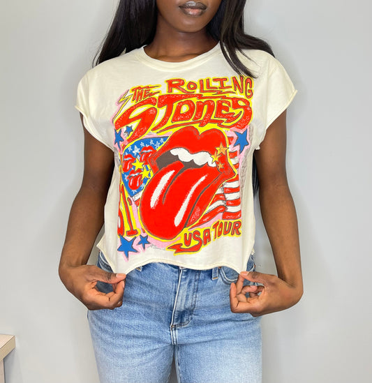 Front close-up of a model wearing the cropped Rolling Stones USA Tour tee, hands gently pulling the hem to show the raw edge and iconic red tongue logo with stars and stripes.
