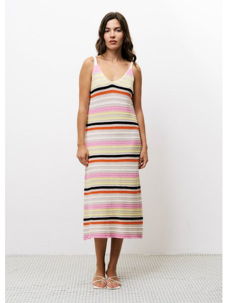Model wearing the Alcathea Dress, shown from the front, featuring a V-neckline, sleeveless design, and a fitted silhouette with multicolored horizontal stripes in shades of pink, yellow, orange, black, and ivory. The dress falls to mid-calf and is styled with white strappy sandals against a clean white background.