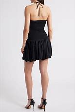 Back view of a woman wearing the Faye Mini Dress in black, featuring a halter neck with tie closure and a voluminous bubble skirt, styled with black strappy heels against a plain light background.